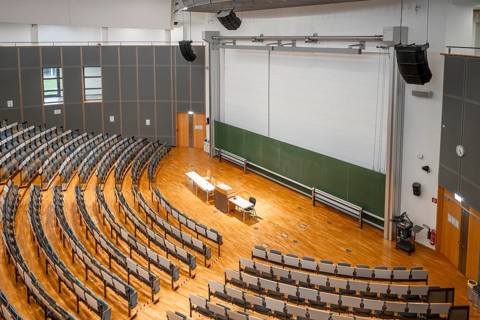 View from above into an empty lecture theatre with rows of seats and lectern, interior photo,