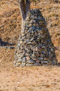 Closeup of pile of stones in the shape of an upside down cone in front of a tree in public road