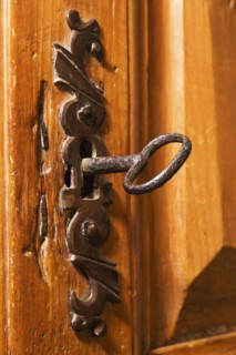 Close-up of antique metal key in keyhole of ornate door lock on wooden armoire in living room