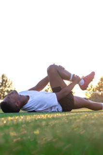Football player with leg pain on the field. Football player lying on the grass rubbing his leg.