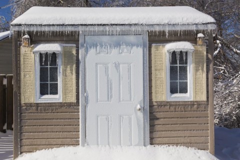 Storage shed facade covered in thick ice and snow in residential backyard after ice storm in early