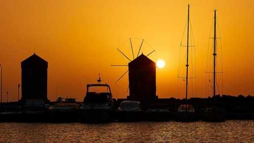 Harbour view with windmills and boat silhouettes at a bright sunrise, twilight, Mandraki Harbour,