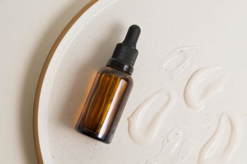 Blank amber glass essential oil (serum) bottle with pipette on cream background. Skin care concept