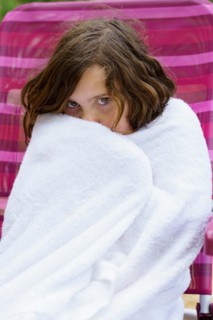 Pretty eight-year-old girl sitting on a chair wrapped in a white towel after getting out of the