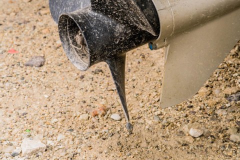Closeup of black propeller and rudder shaft of outboard engine used to power small boat in South