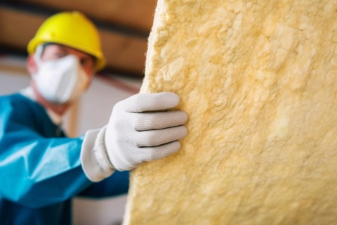 Construction worker installing mineral wool filling used as isolation material in walls. KI