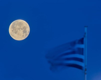 A full moon next to a waving Greek flag in the blue hour, twilight, Mandraki Oat, Rhodes,
