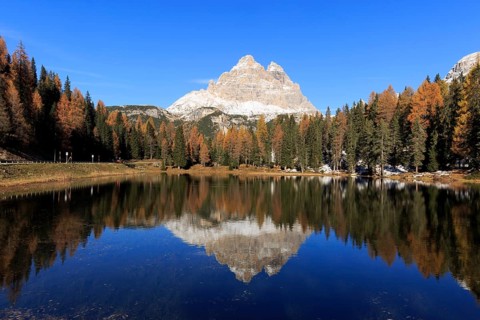 Calm water surface of a lake in the midst of autumnal forests reflects a mountain, Italy, South