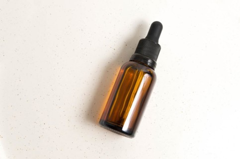 Blank amber glass essential oil (serum) bottle with pipette on cream background. Skin care concept
