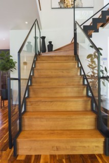Black powder coated steel L-shaped staircase with stained and varnished wooden steps and tempered