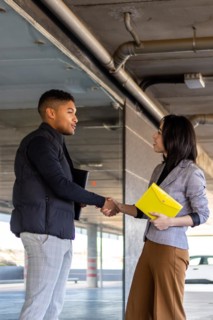 Woman in formal suit shaking hands with casual man outdoors. Business woman shaking hands with guy