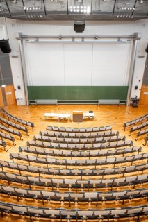 View from above into an empty lecture theatre with rows of seats and lectern, interior photo,