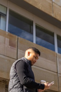Vertical portrait of a latin man in smart casual clothes texting on the street outside her office