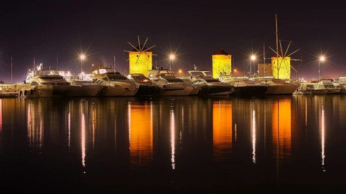 Oat at night with illuminated windmills and yachts reflected in the water, twilight, Mandraki