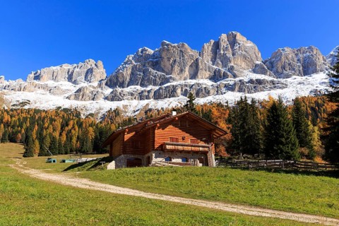 Red roof of a wooden hut in front of a wide mountain panorama under a blue sky, Italy, Alto Adige,
