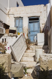 Discarded items in front yard of abandoned traditional house with blue wooden entrance door,