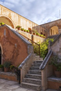 Stone staircase leading to cloister and wall with various plants in terracotta planters in inner