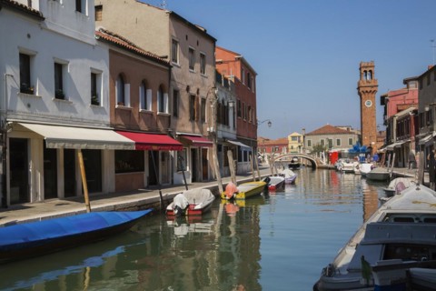 Moored boats on canal with colourful residential buildings, houses, shops and clock tower in San