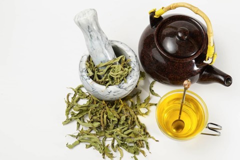 Lemon verbena infusion in a glass cup with a marble mortar and pestle and a ceramic teapot with