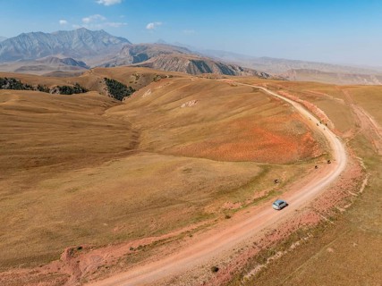 Moldo-Ashuu Pass, car on road between yellow hills, near Baetov, Naryn region, Kyrgyzstan, Asia