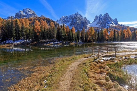 A hiking trail leads to a quiet lake surrounded by autumnal trees and mountains, Italy, South