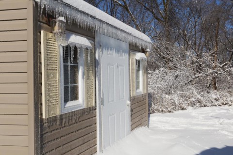 Storage shed facade covered in thick ice and snow in residential backyard after ice storm in early