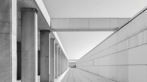 A symmetrical greyscale image of a corridor lined with columns, AI generated