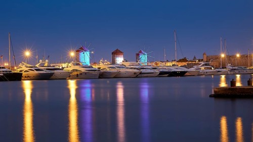Lively marina at night with illuminated windmills and reflections in the water, twilight, Mandraki