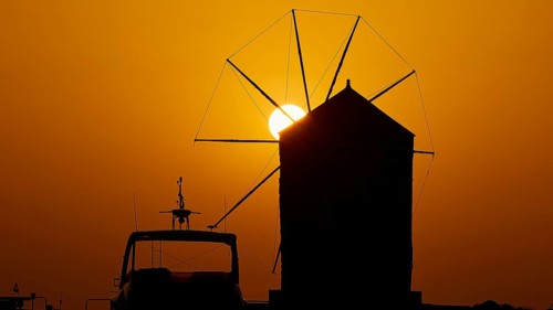 Silhouette of a windmill against the background of an orange sunrise sky, twilight, Mandraki Oat,