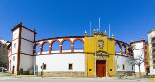 Bright historic building with red accents and coat of arms under a clear blue sky in an urban