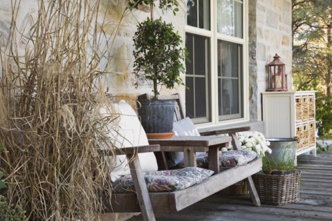 Weathered wood sitting bench with cushions plus various plants, herbs including ornamental grass