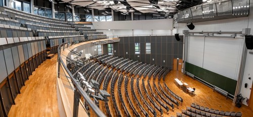 View from the gallery into an empty lecture theatre with rows of seats and lectern, interior photo,