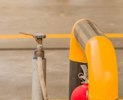 White hose attached to water faucet with a pull handle next to yellow and black guardrail in