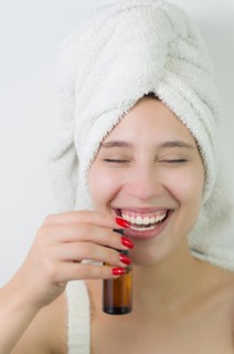 Happy young woman with towel on head holding amber glass bottle of skin serum. Beautiful young