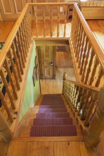Looking down staircase with maple wood railings and pine wood steps covered with multi-coloured