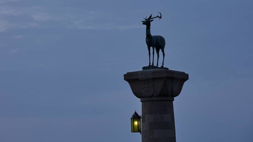 Deer statue on column with illuminated lantern at dusk, Mandraki Oat, Rhodes, Dodecanese, Greek