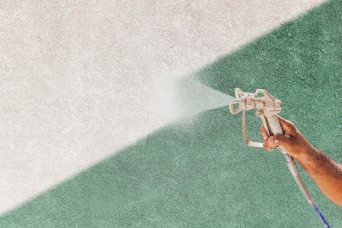 Professional spray painter holding spray gun spraying white paint over teal stucco surface