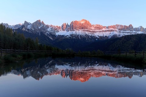 Early morning light illuminates a mountain range reflected in a still lake, Trentino-Alto Adige,