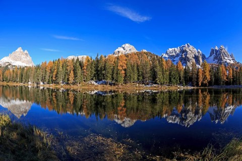 A panoramic picture of a mountain lake, surrounded by forests in autumn dress with a clear