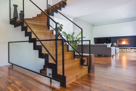 Black powder coated steel L-shaped staircase with stained and varnished wooden steps and tempered