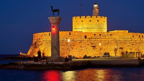 Night view of an old fortress with red lights and a sculpture by the sea, night shot, deer statue,
