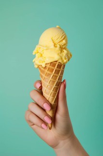 Hand holding yellow ice cream in cone in front of green studio background. KI generiert, generiert,