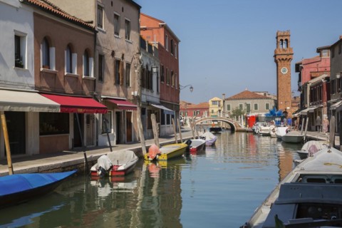 Moored boats on canal with colourful residential buildings, houses, shops and clock tower in San