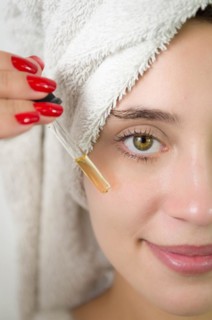 Happy young woman applying serum on her face with her eyes open. Beautiful young Brazilian woman