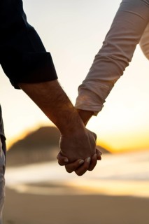 Vertical close-up of lovers holding hands gazing sunset on the beach