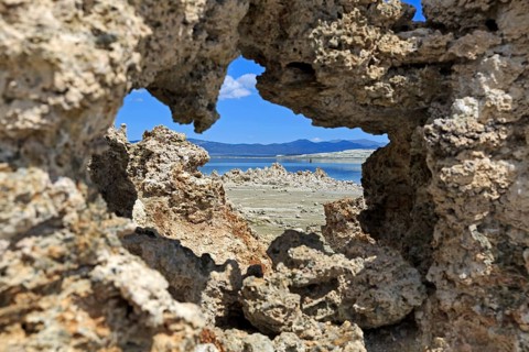 View through a natural rock opening to a quiet landscape with blue sky in the background, Mono