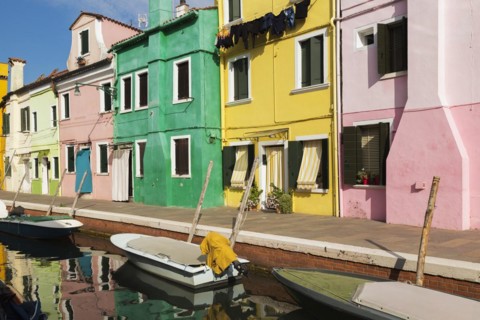 Moored boats on canal lined with pink, yellow and green stucco houses decorated with striped