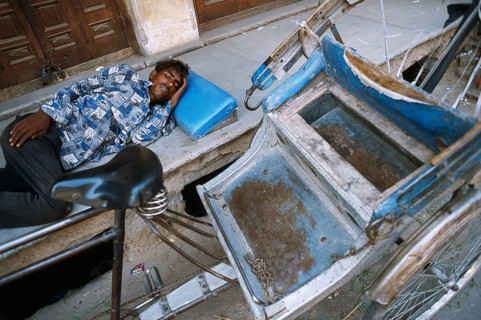 Man sleeping on the sidewalk. In the foreground, his rickshaw. Ajmer, Rajasthan, India, He is