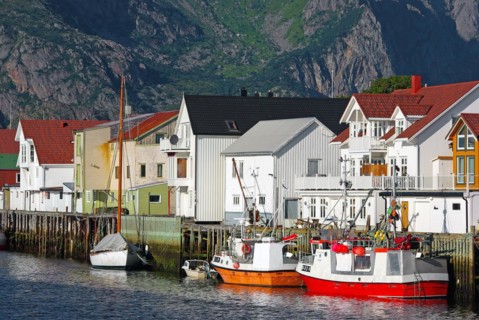 Fishing boats in front of wooden houses and high mountains in a small harbour, Idyll, Henningsvaer,