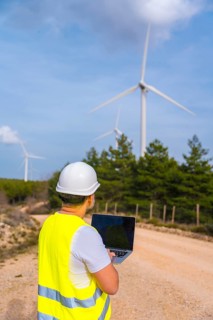 Vertical photo with copy space of the rear view of worker of a wind energy park using laptop